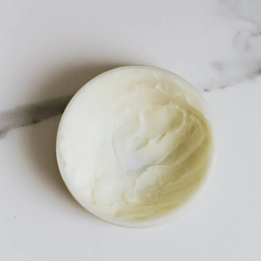 Öppen burk med krämigt kroppssmör på ljust marmor